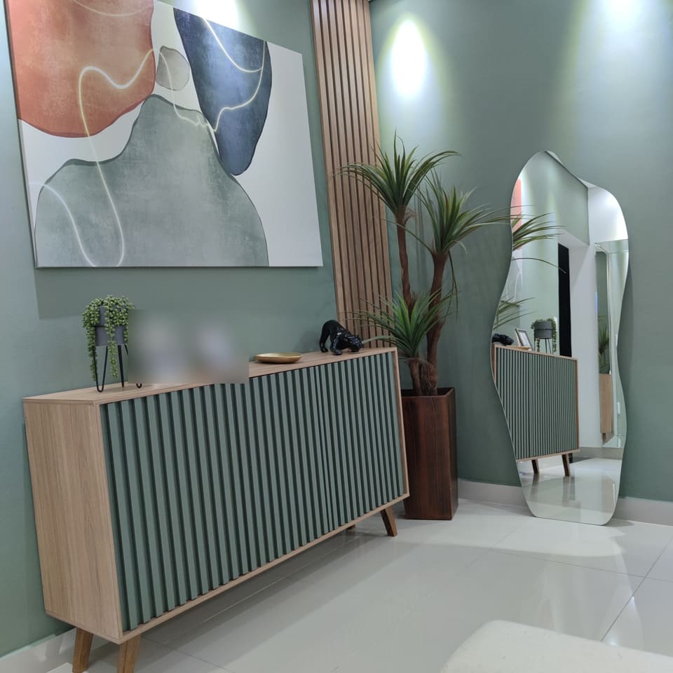 Hall com parede verde, quadro, aparador ripado, planta e espelho orgânico de corpo inteiro no canto