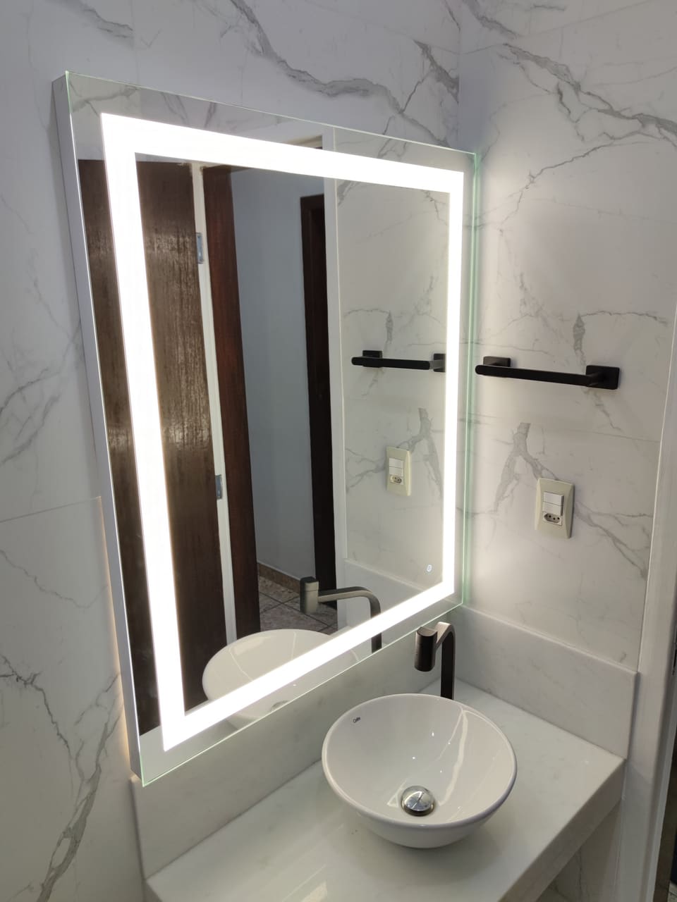 Espelho retangular com LED touch aceso sobre cuba redonda de apoio em banheiro com porcelanato marmorizado