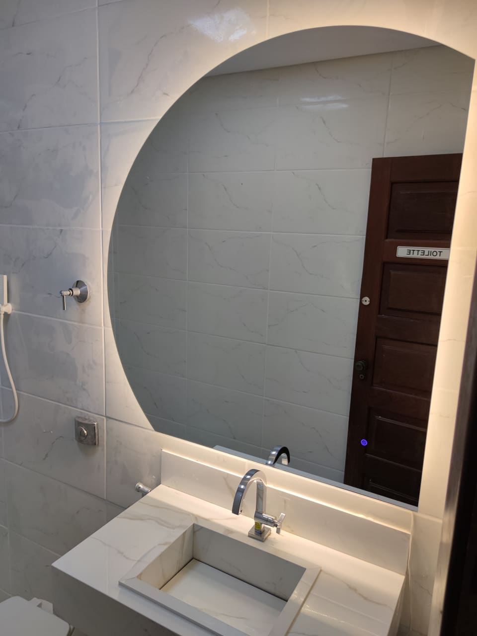 Espelho orgânico iluminado em lavabo de porcelanato claro, com LED quente atrás do vidro