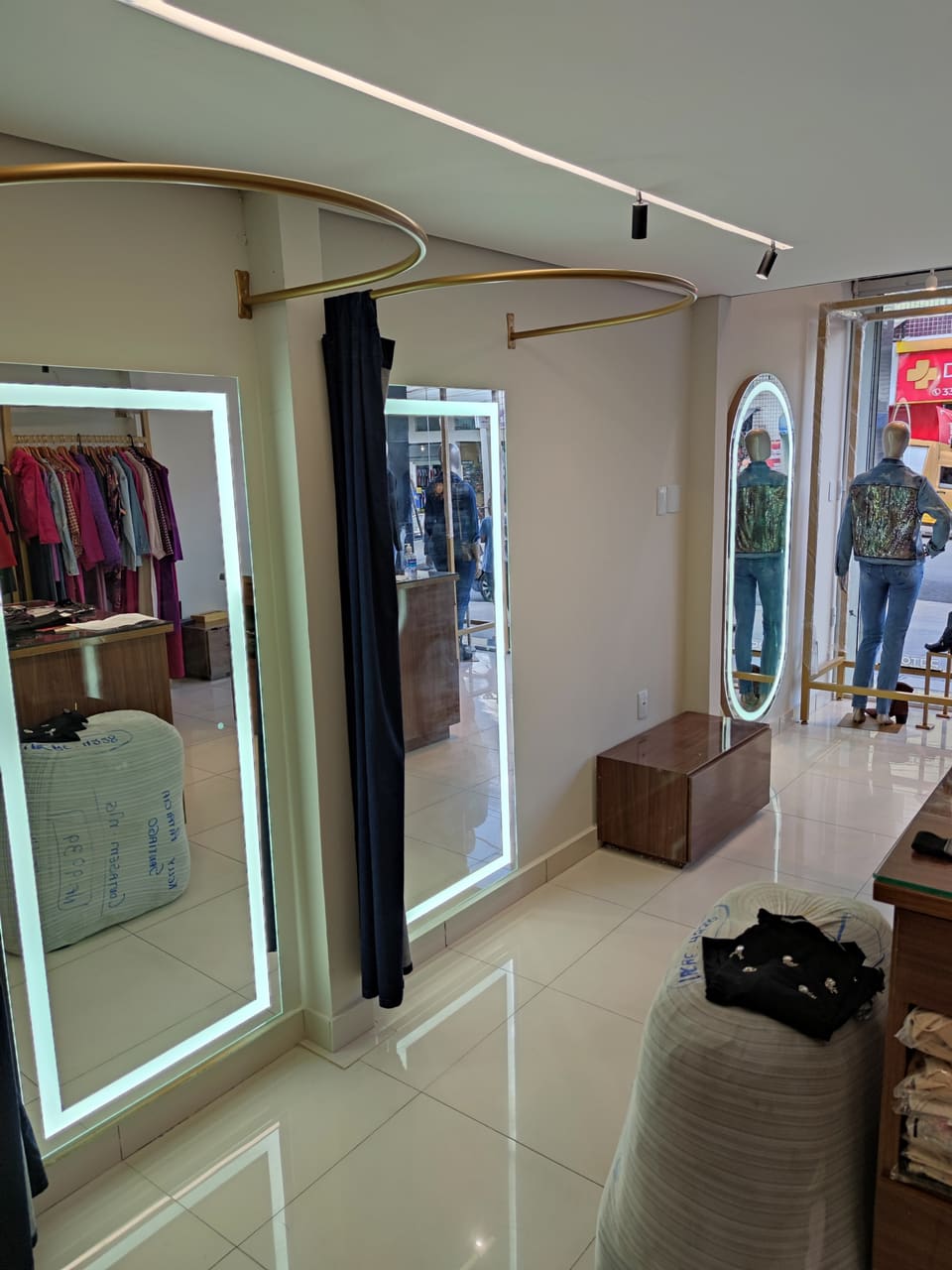 Loja de roupas com espelhos retangulares de corpo inteiro com LED nos provadores e espelho oval com luz perto da vitrine