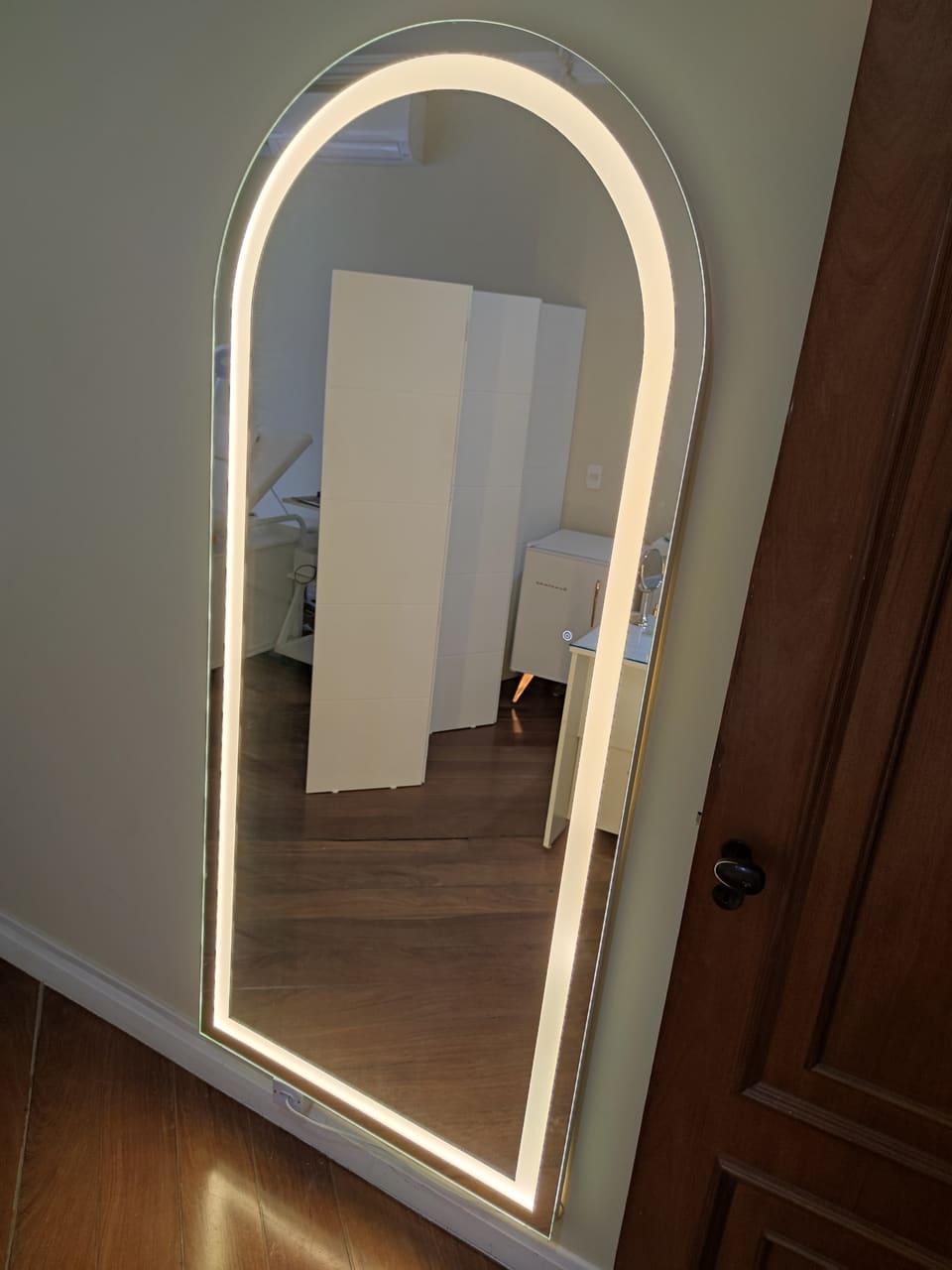 Espelho em arco de corpo inteiro com LED frontal aceso em quarto com piso de madeira